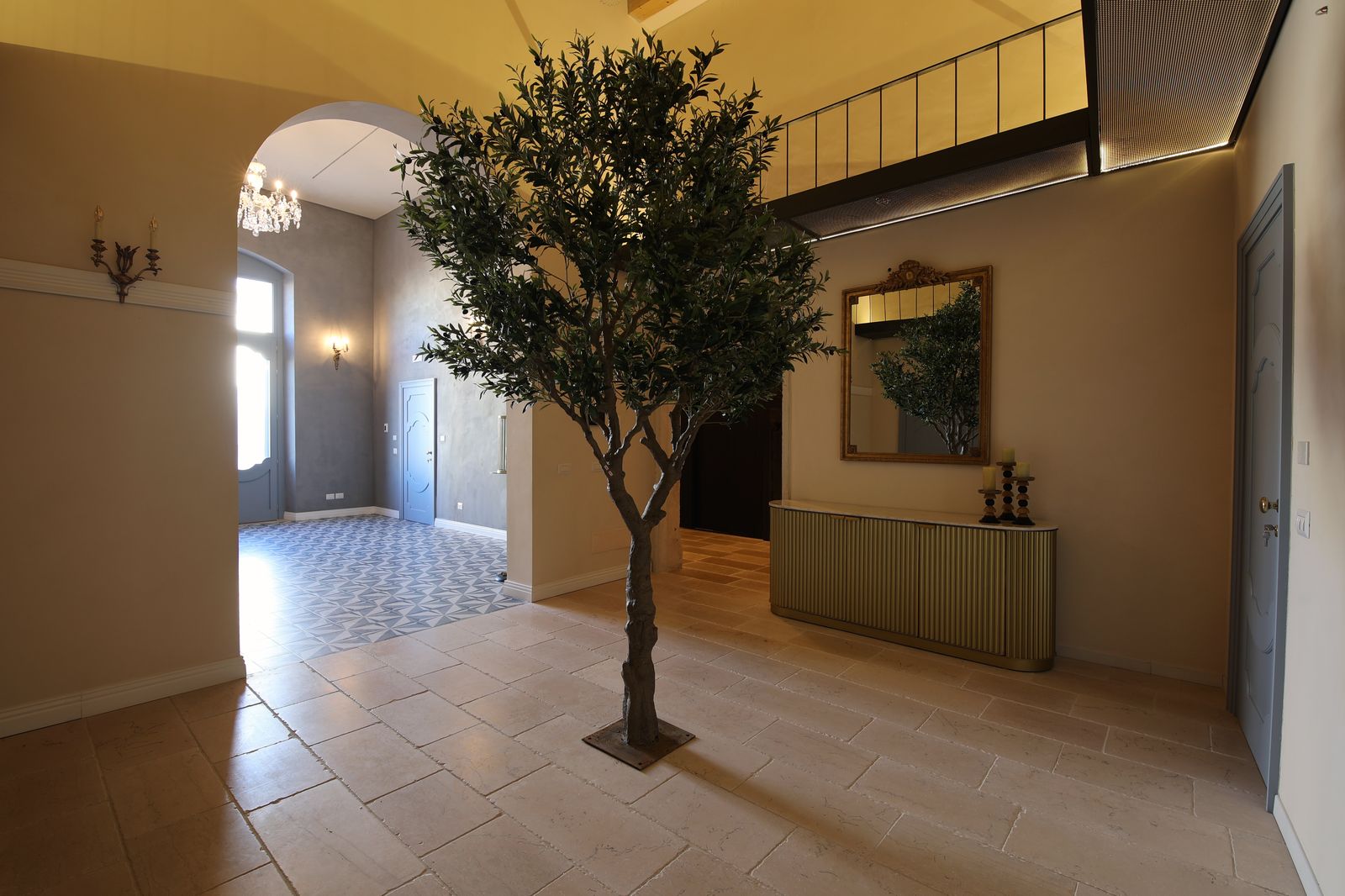 Entrance hall of the palazzo, with a stone-flagged floor, an olive tree at its centre and a fluted gold console beneath a gilt mirror.