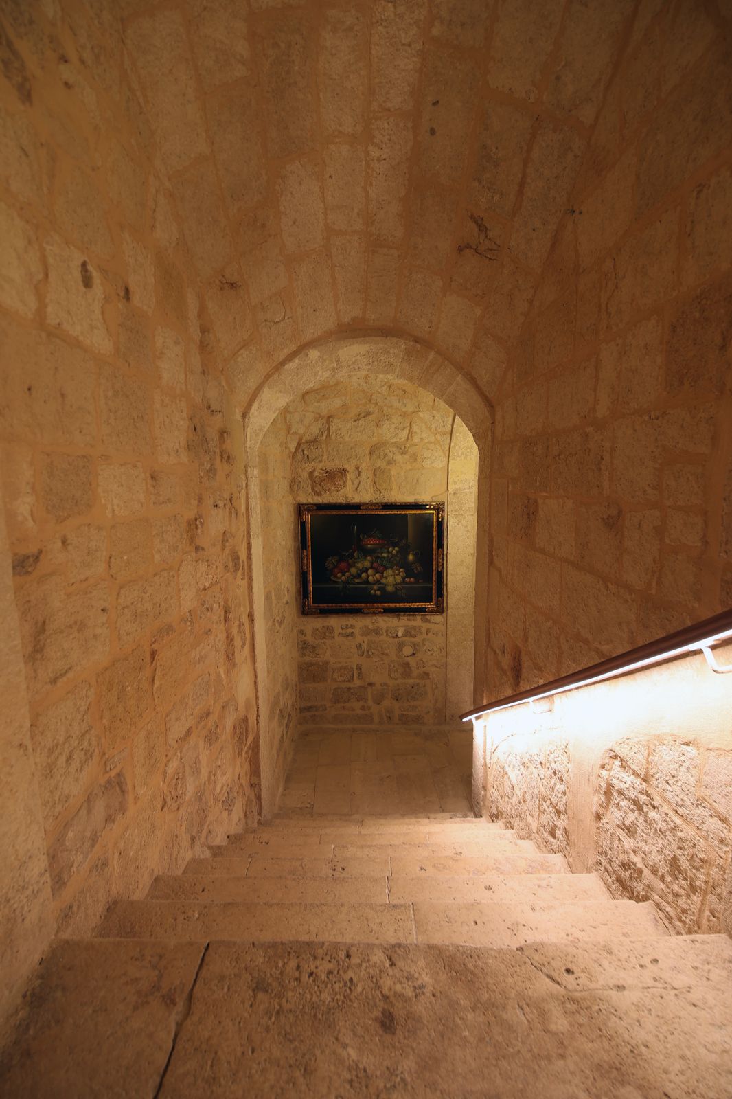 Stone staircase descending beneath a vaulted ceiling towards a framed still life set in an arched alcove.