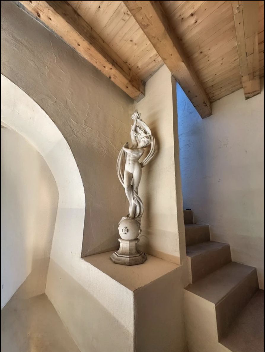 A carved female statue standing in a plastered niche beneath an exposed wooden beam ceiling.