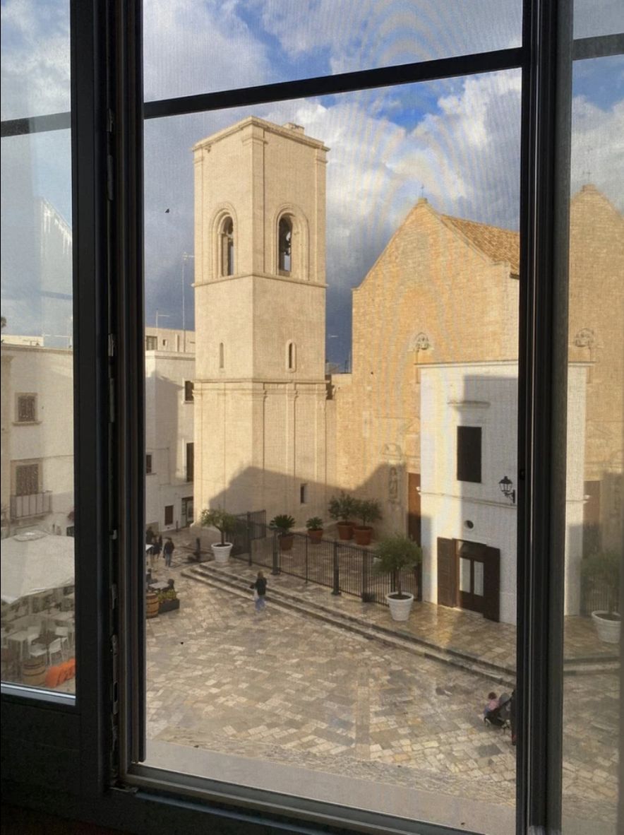 View from a palazzo window across the piazza to Polignano a Mare's stone bell tower and church.