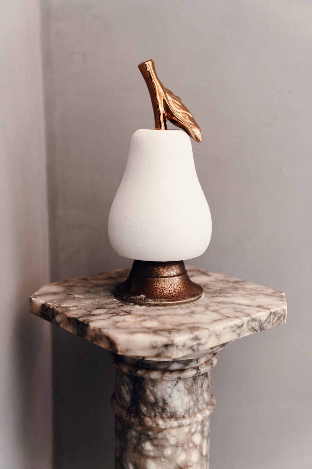 A white pear-shaped lamp with a bronze stem and leaf, standing on a marble pedestal.