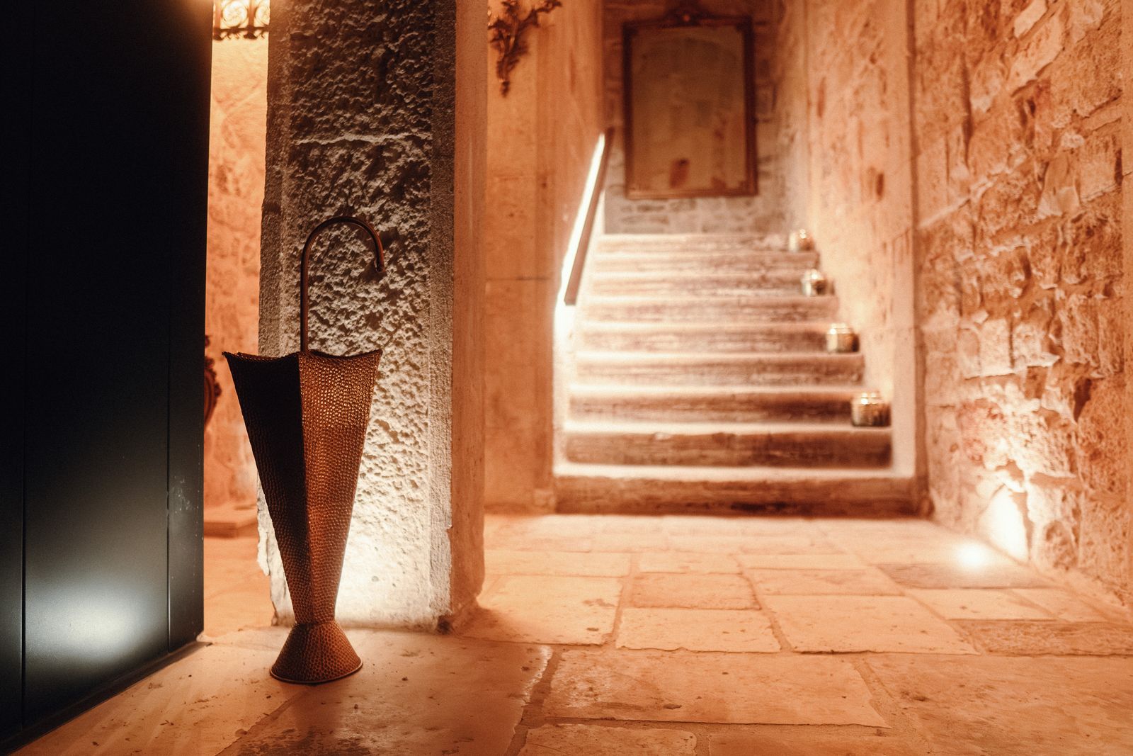 The palazzo's stone staircase lit from below, with a tall metal umbrella stand beside a stone pillar.