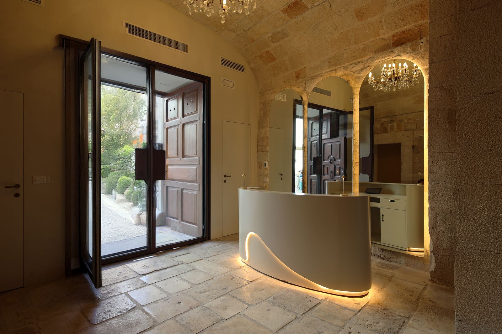 Reception desk with a curved, softly lit counter under the palazzo's vaulted stone ceiling, the original wooden door open to the garden.