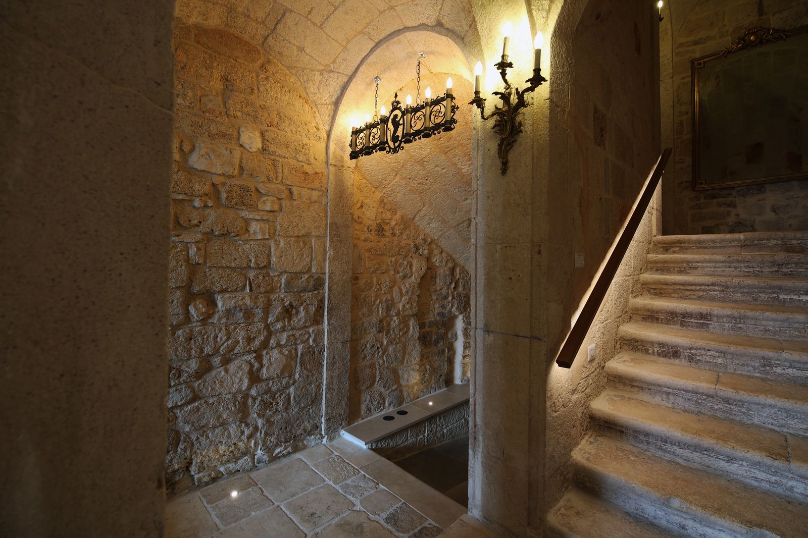 The palazzo's original stone staircase, lit by a wrought-iron chandelier and a gilded wall sconce.