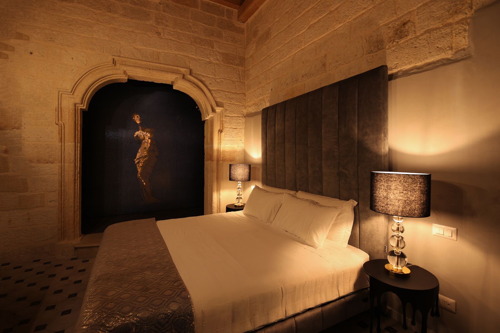 Guest room with exposed stone walls and a backlit Venus figure set in a carved stone niche behind the bed.