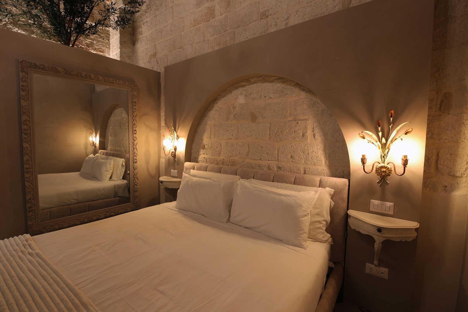 The bed beneath the stone arch and the brass wall lamps.