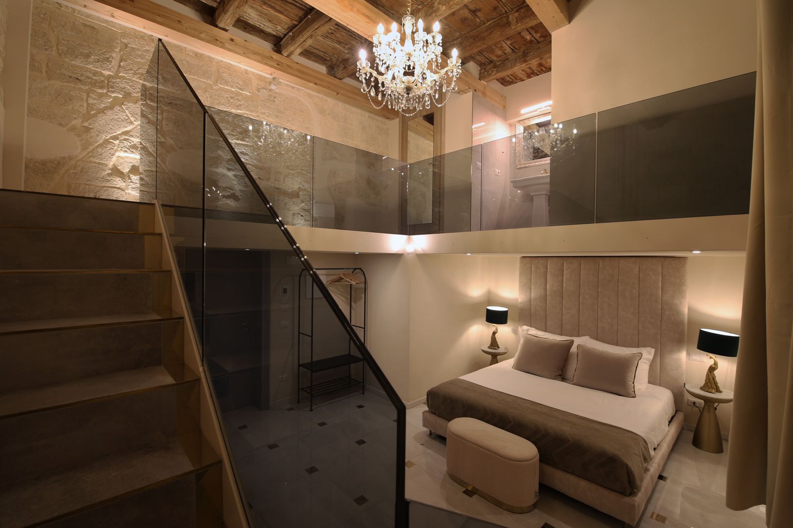 Reflection Junior Suite: a double-height room with a crystal chandelier hanging from the original beamed ceiling and a staircase up to the mezzanine.