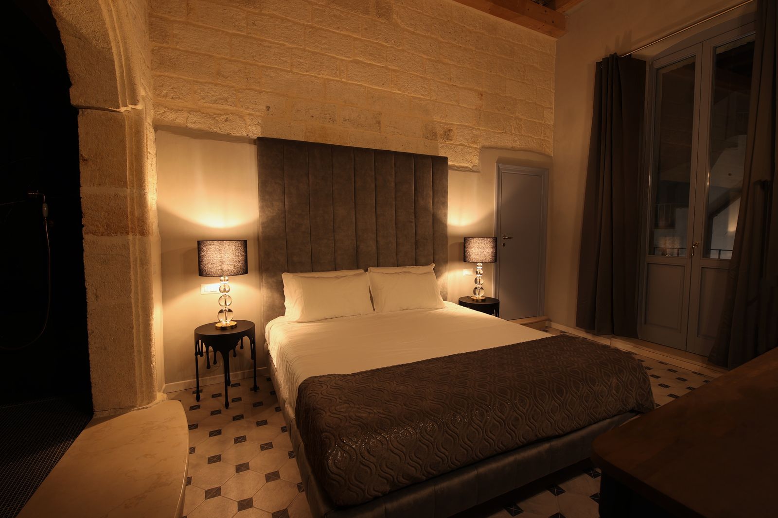 Venus Deluxe Room: a bed against exposed stone beneath a high ceiling, with an arched stone opening through to the bathroom.
