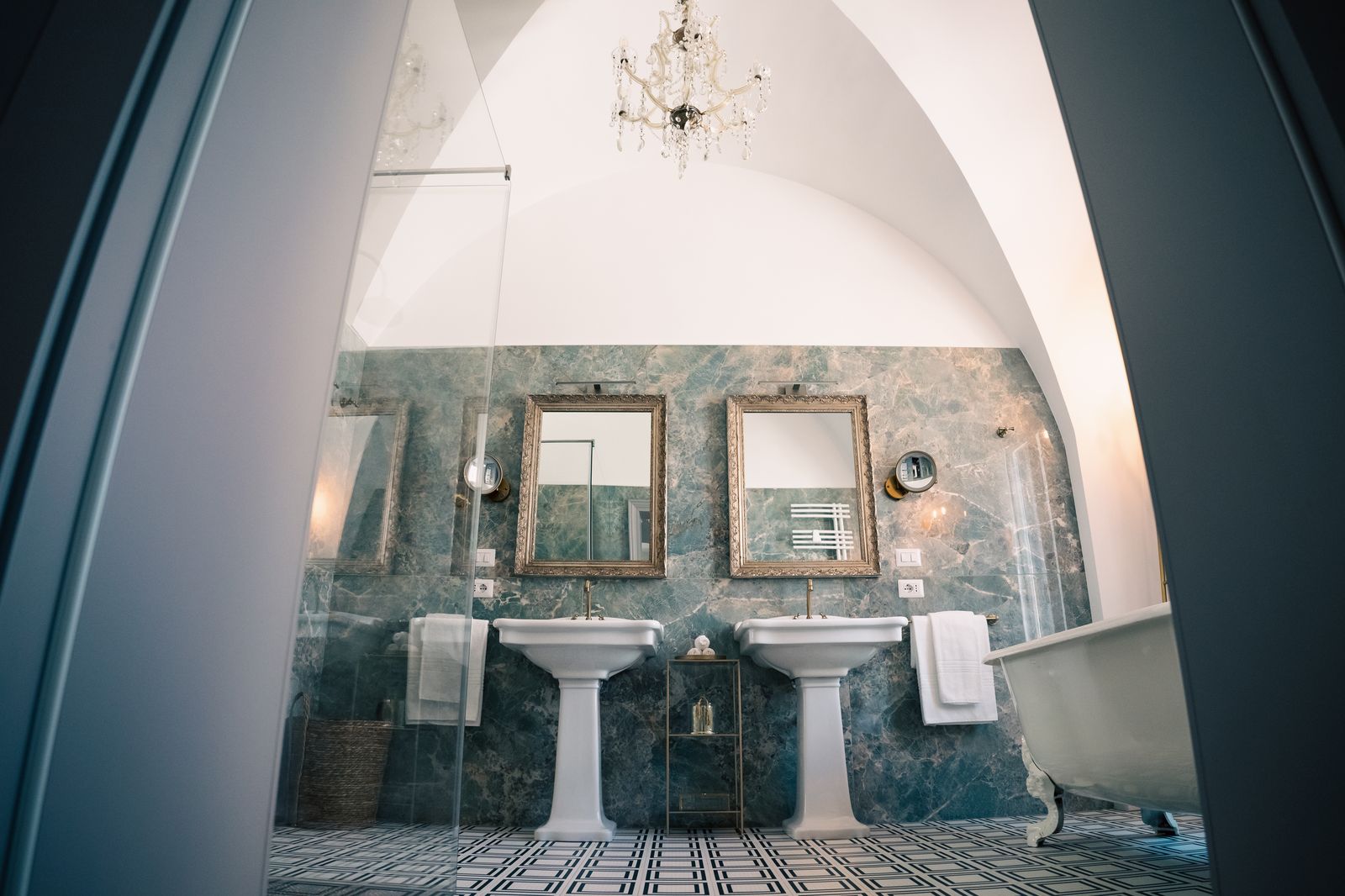 Duchess Grande Suite: the bathroom, with green marble walls, twin pedestal basins, a free-standing tub and a chandelier under the vaulted ceiling.