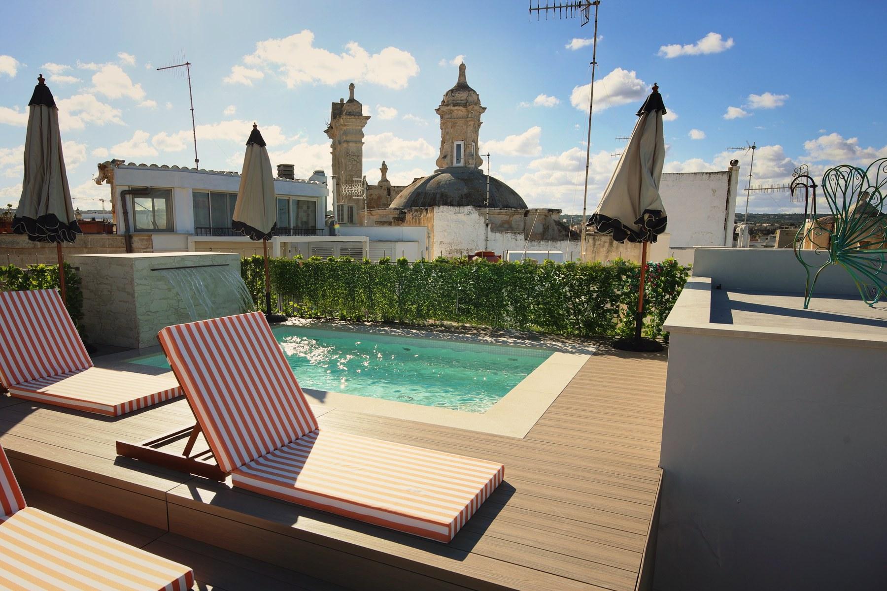 Striped sun loungers and parasols around the heated rooftop pool, with Polignano's church dome and bell tower behind.