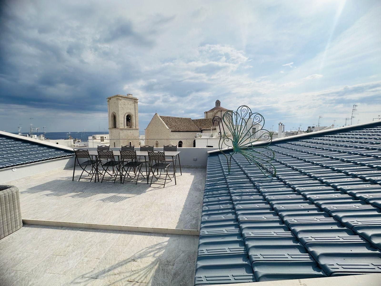 A long dining table set out on the rooftop terrace, facing Polignano's bell tower, church and the sea.
