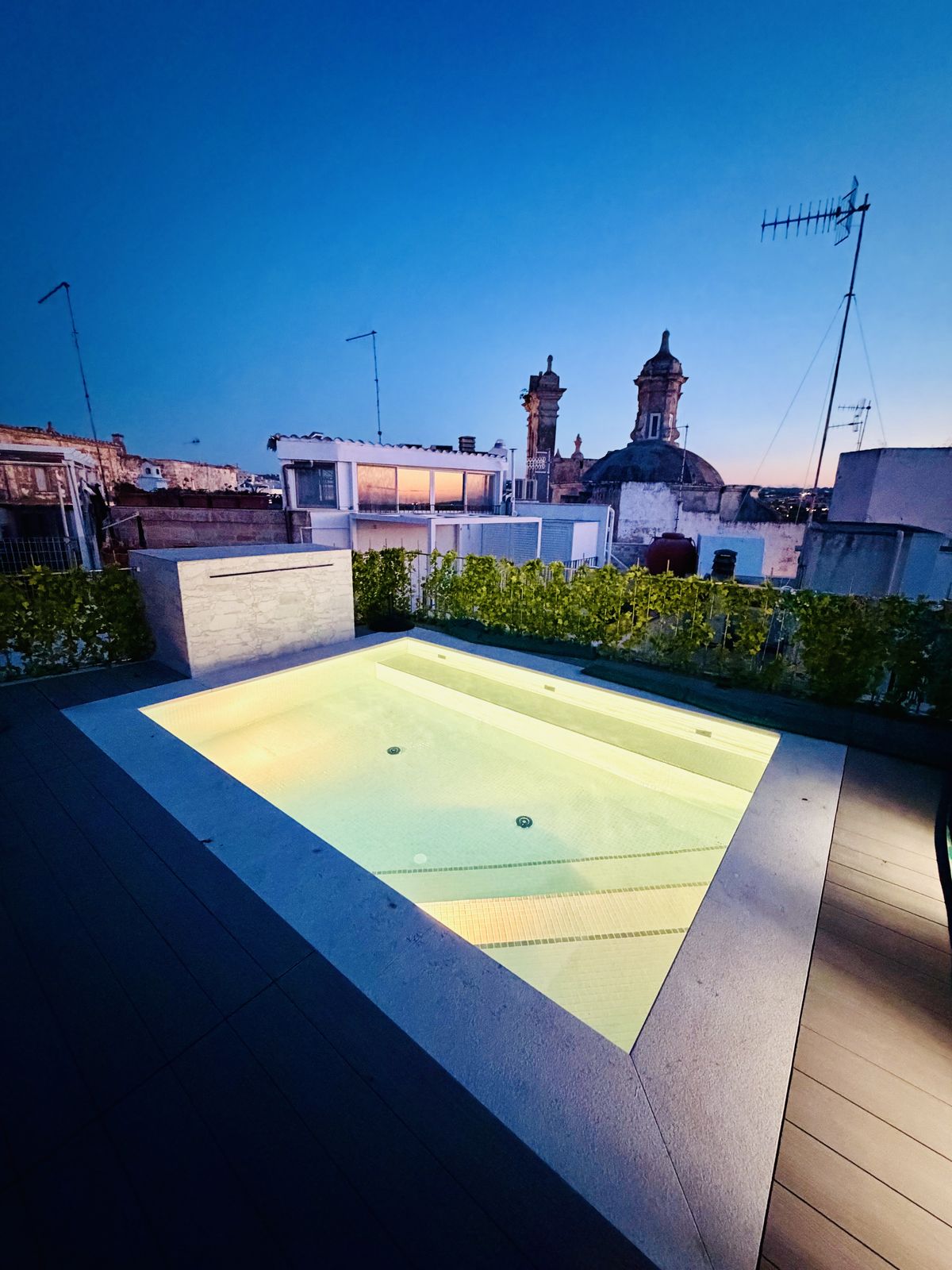 The rooftop pool lit from within at dusk, with the domes of Polignano's old town against a deep blue sky.